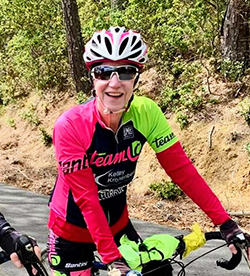 Linda Curtis smiling on her bike, wearing long sleeves, sunglasses, and a helmet.