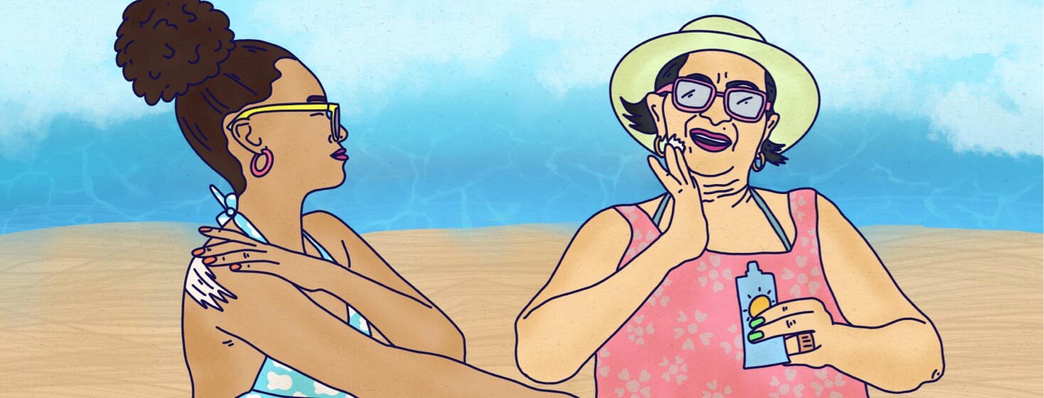 Elder Mother And adult daughter sitting on the beach in their beachwear enjoying the sun while applying sunscreen.